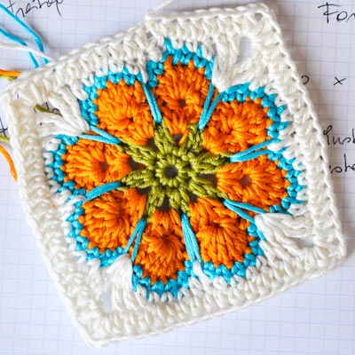 This orange crocheted flower on this granny square looks great with the blue yarn outline. 